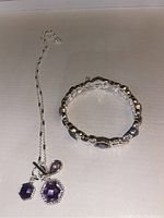 Photo showing tanzanite-colored stone necklace with silver-tone chain next to matching bracelet.