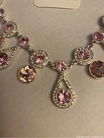 Close-up image showing pink crystals in various shapes set in silver-tone metal on the necklace.