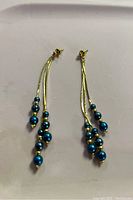 Pair of gold-tone drop earrings with several blue beads each, shown against a white background.