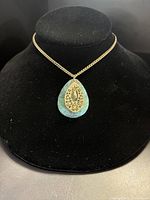 Photo showing the gold-tone necklace with a turquoise teardrop pendant featuring an intricate gold filigree detail, displayed on black velvet bust.