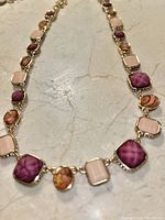 Close-up view of the necklace showing the purple tourmaline, orange alexandrite, and light pink stones set in gold bezels on a marble background.