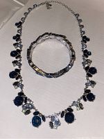 Necklace and bracelet set displayed on flat surface, showing deep blue sapphire and iolite gemstones, clear and pale yellow accent stones, silver-tone metal.