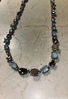 Close-up photo of a delicate necklace arranged on a stone surface, with Alexandrite and Topaz stones linked in an alternating pattern.