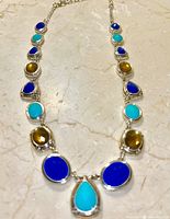 Front view of the necklace displayed laying on a marble surface showing the arrangement of lapis lazuli, topaz, and turquoise stones in teardrop and oval shapes.