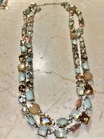 Top view of the double-strand necklace on a marble surface showing various colored gemstones and silver-tone metal chain.