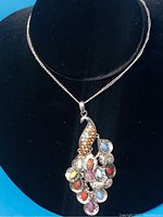 Full front view of the peacock pendant necklace with multicolored gems on a silver-tone chain displayed on a black velvet bust.