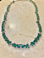 Full length view of silver-tone necklace with green crystals laid out on marble surface.