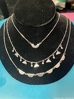 Silver three-tier necklace displayed on black bust showing different pendants and extended chain