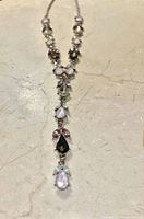 Close-up of silver necklace with kunzite and other gemstone accents laid flat on a stone surface.