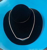 Silver V-shaped pendant necklace on a black velvet bust against a blue background.