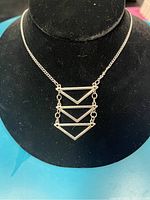 Silver necklace displayed on black velvet holder showing three connected inverted triangles pendant and chain.