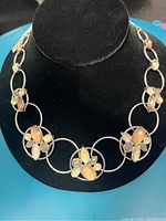 Silver necklace displayed on a black necklace stand showing the front view with flower-shaped clusters of brown topaz and peridot stones.