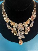 Photo showing a necklace with multiple smoked topaz and lilac opal stones in a floral metal setting, displayed on a black bust.
