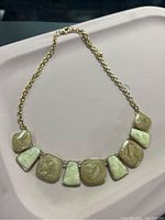 Front view of gold-tone necklace featuring seven marbled beige and cream swirl panels on gold link chain.