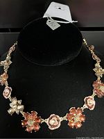 Close-up photo of the floral topaz-colored stone necklace on a black display bust showing flower-shaped settings with amber, light pink, and clear stones and a rose gold-tone chain.