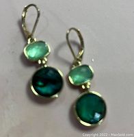 Pair of gold earrings with green peridot and blue-green round stones, shown against a light background.