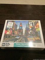 Front view of one sealed 1000-piece puzzle box showing a Times Square image with taxis and cityscape.