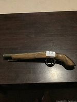 Photo of full replica 18th century flintlock pistol showing wooden stock, metal barrel, and trigger guard on dark wooden surface.