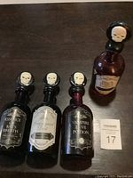 All four decorative poison bottles arranged upright, showing black skull-topped stoppers and labels on each bottle.