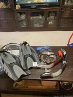 Photo showing the flippers, masks, and snorkels arranged on a wooden table in a living room setting.