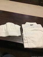 Image showing folded white chef coat and matching pleated chef hat placed on a dark wooden surface.