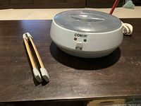 Full view of Conair heating unit with wooden stone tongs on table.