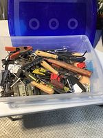 Plastic container holding assorted hand tools including clamps, screwdrivers, and wrenches.