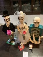 Full set of Day of the Dead themed bride and groom figurines alongside skeletal hand bottle and small figurines on table.