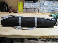 Full view of the black drawing tube lying horizontally with gray shoulder strap and trim on a workbench.