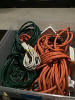 Plastic bin containing multiple orange, green and white extension cords coiled and bundled
