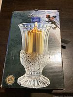 Boxed Longchamp large hurricane vase with gold candle pictured on front of packaging.
