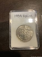 Full front view of coin in clear plastic protective case with label '1984 DOLLAR'.