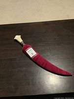 Full view of the jambiya in its red sheath on a dark surface