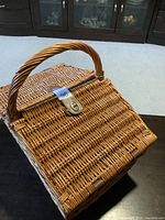 Closed woven wicker picnic basket with single handle and leather strap lock on the lid