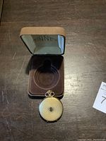 Finnex branded protective case open, showing interior and gold-tone pocket watch closed outside case