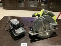 Overall shot of the RYOBI cordless circular saw with battery and charger on a table.