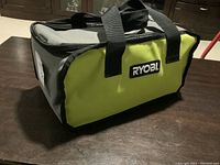RYOBI branded carrying bag for tool, showing handles and fabric material with lime green and gray colors.