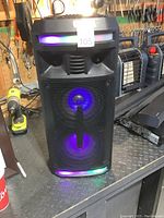 Front view of black Sylvania SP917 speaker showing two 6.5-inch speaker cones glowing blue with multicolor LED light strips at top and bottom front.