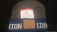 Close-up of toque cuff showing blue knit with white 'EDMONTON' text and brown leather patch with signature and name 'Jari Kurri'. Molson Canadian promotional tag attached.