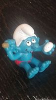 Photo of vintage 1980s Smurf figure sitting, blue with white hat, red swimsuit, holding sponge and soap.
