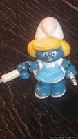 Full body front view of vintage 1980s nurse Smurfette figure in light blue dress holding syringe and medical accessory