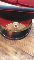 Front view of vintage Soviet officer cap showing red band, gold laurel leaf insignia with red star USSR emblem, gold braided cord, and shiny black visor.