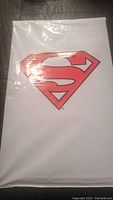 Front view of the sealed comic book bag showing the Superman logo in red and black on a white background, indicating the comic is bagged and sealed.