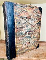 Front cover showing half leather binding and marbled paper boards on wooden shelf