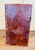 Front cover of a very old leather bound book, dark brown leather with metal clasps and no hinges.