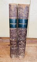Spines of two volumes showing leather spines and embossed labels with text 'Commentary' and 'Genesis to Deuteronomy'. The leather is worn and scuffed.