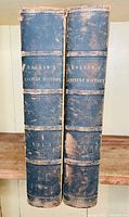 Two leather bound volumes with worn spines labeled Rollin's Ancient History Volume I and Volume II.