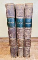 Three antique volumes titled 'Commentary' with browned leather spines and green labels on a wooden surface.