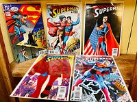 Five Superman comics arranged on a table showing full front covers, each comic is in excellent condition in protective bag and board.