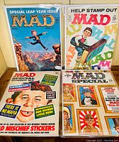 Four bagged and boarded Mad magazines arranged on a surface showing colorful, satirical cover art and titles.